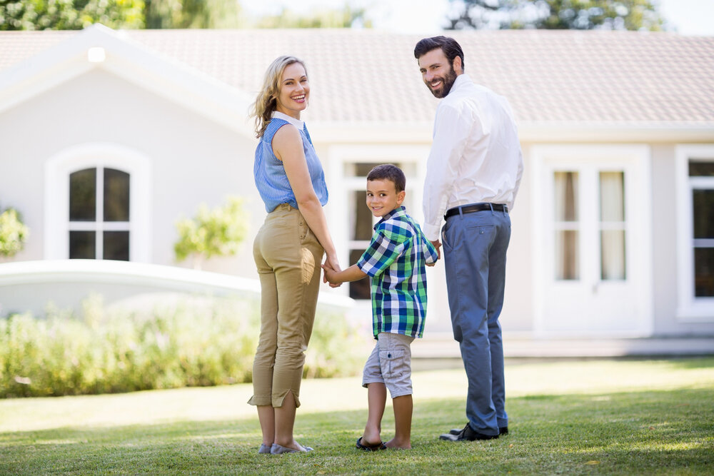 Portrait Of Parents And Son Standing In Garden Smiling In Front Of House